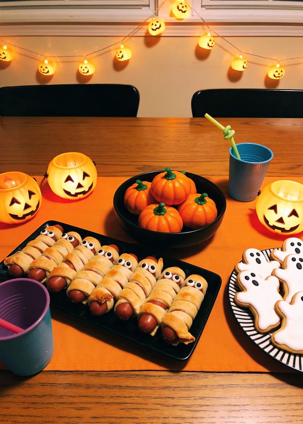 A homemade Halloween table with mummy hot dogs and pumpkin snacks